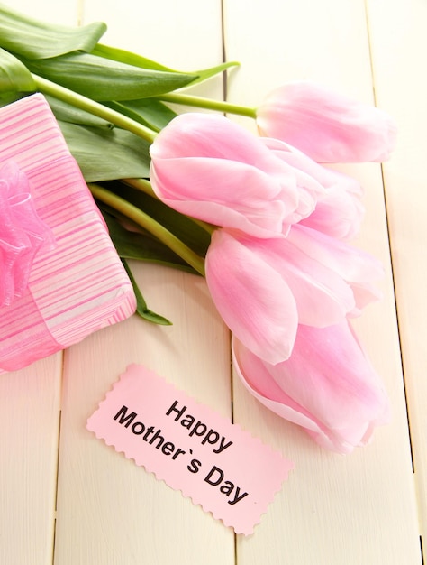 Foto schöner blumenstrauß aus rosa tulpen und geschenk zum muttertag auf weißem holzhintergrund