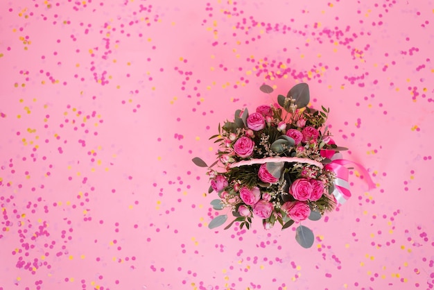 Schöner Blumenstrauß aus rosafarbenen Rosen und Eukalyptuszweigen in einem Geschenkkorb auf rosafarbenem Hintergrund mit Konfetti zum Geburtstag Valentinstag oder Muttertag Draufsicht aus dem Kopierbereich