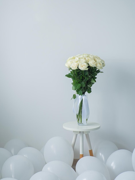 Schöner Blumenstrauß aus weißen blühenden Rosen in Glasvase auf rundem Tisch