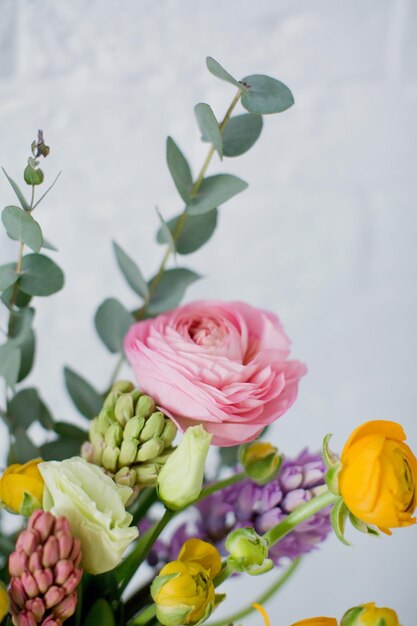 Schöner Blumenstrauß mit orangefarbenen und rosa Ranunkeln, Eukalyptus und Hyazinthen in einer grünen Vase auf weißem Hintergrund