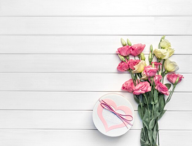 Schöner Blumenstrauß von rosa, lila, gelben Eustoma-Blumen und handgemachter Geschenkbox auf weißem hölzernem Hintergrund. Speicherplatz kopieren, Draufsicht