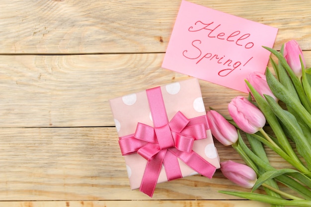 Schöner Blumenstrauß von rosa Tulpenblumen, Geschenkbox und Text hallo Frühling auf Papier auf einer natürlichen Holzoberfläche