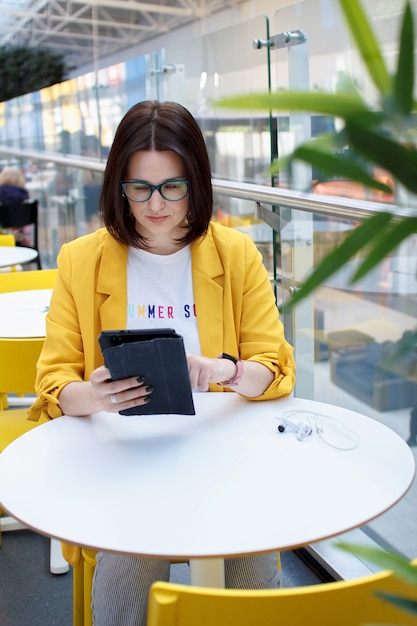 Schöner Brunette in einer gelben Jacke, die an einer digitalen Tablette arbeitet