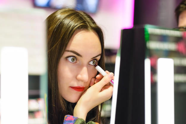 Schöner Brunette mit rotem Lippenstift prüft die Lidschatten im Schönheitsspeicher