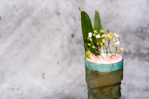 Schöner Cocktail, garniert mit Kalk und Blumen auf Betongrund