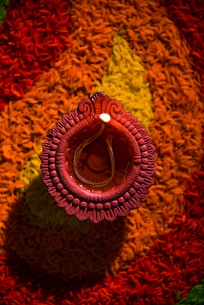 Foto schöner diwali-gruß mit diya- oder tonöllampe beleuchtet und über rangoli angeordnet, hergestellt aus mehrfarbigen reiskörnern, selektiver fokus