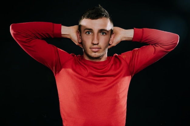 Schöner europäischer Sportler, der rote Sportbekleidung trägt und nach hartem Training auf dunklem Hintergrund posiert Sportlicher Mann, der sich mit den Händen auf dem Kopf streckt Gesunder Fitness-Lifestyle Sportmotivation