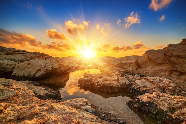 Schöner farbenfroher Sonnenuntergang in der Nähe des Meeres auf Zypern mit dramatischen Wolken und Felsbrocken Spiegelungen im Wasser Schönheitswelt natürlicher Reisehintergrund im Freien