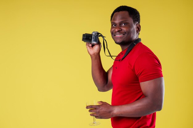 Schöner Fotograf glücklicher junger afrikanischer Mann Kenia Afrika Tourist isoliert gelber Wandhintergrund mit Tickets mit Pass und Cocktailglas und Fotokamera Reise um die Welt