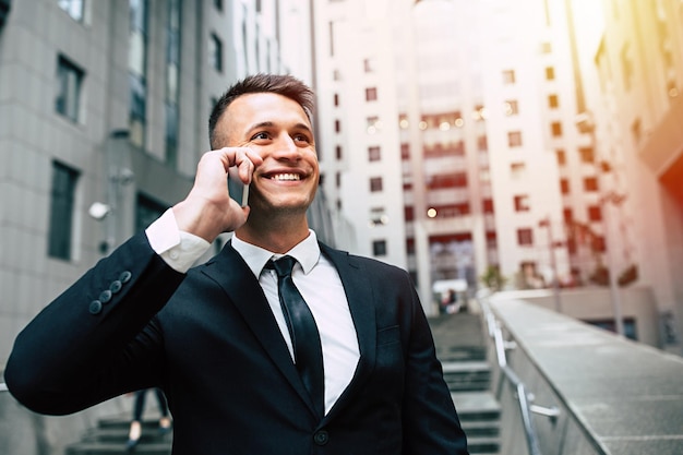 Schöner, fröhlicher Geschäftsmann in elegantem schwarzem Anzug und Krawatte, der am Telefon spricht