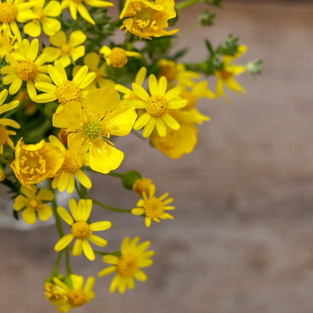 Schöner gelber Blumenstrauß der Blumen steht auf einem hölzernen Hintergrund