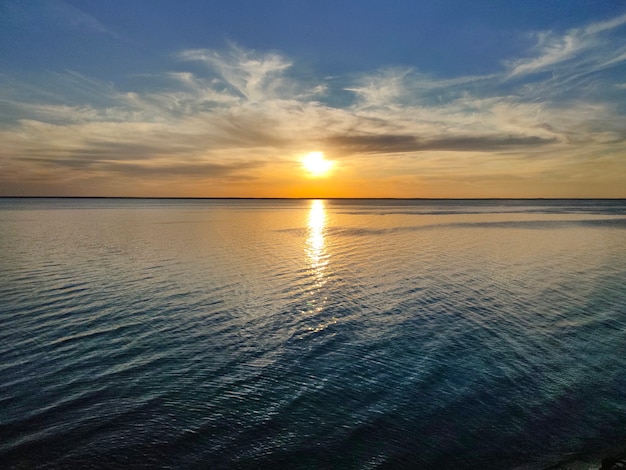 Schöner gelber Sonnenuntergang am Meer und Obloka am blauen Himmel, reflektiert im Seespiegel.