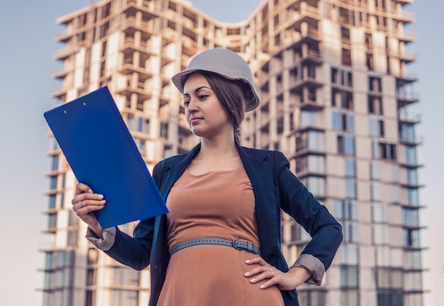 Schöner Geschäftsfraueningenieur steht mit Planpapieren. Bauprojekt ist im Hintergrund