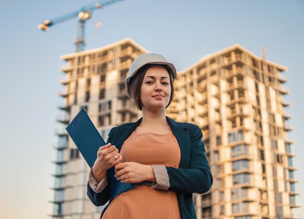 Schöner Geschäftsfraueningenieur steht mit Planpapieren. Bauprojekt mit Kran ist im Hintergrund