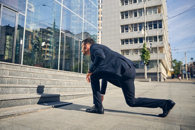 Schöner Geschäftsmann, der aufsteht, nachdem er schwarze Schuhe in der Nähe der Treppe des großen Glasbüros geschnürt hat