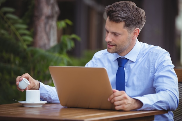 Schöner Geschäftsmann, der Tee beim Verwenden des Laptops hat