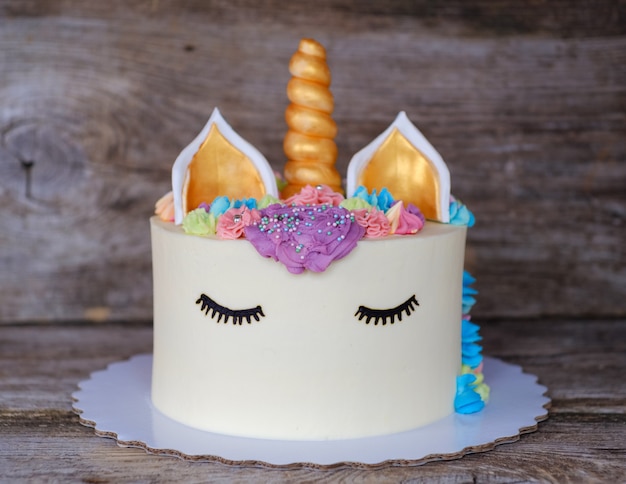 Schöner hausgemachter Kuchen in Form eines Einhorns mit cremefarbenen Blumen auf einem Holztisch