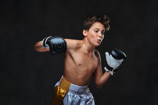 Schöner, hemdloser junger Boxer bei Boxübungen, konzentriert auf den Prozess mit ernster, konzentrierter Gesichtsbehandlung.