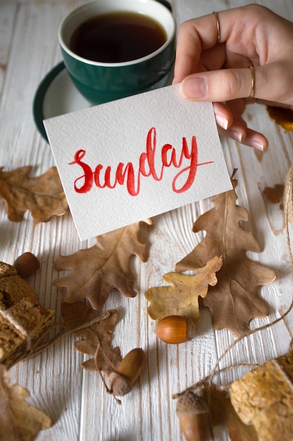 Schöner Herbsthintergrund - Tasse Tee, Biscotti, Herbstblätter und Aufschrift Sonntag