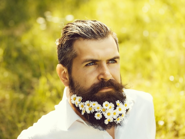 Schöner Hipster-Mann, brünett mit Gänseblümchen im Bart, in schwarzem Hemd mit elegantem Schnurrbart und stilvollem Haar, sonniger Tag im Freien