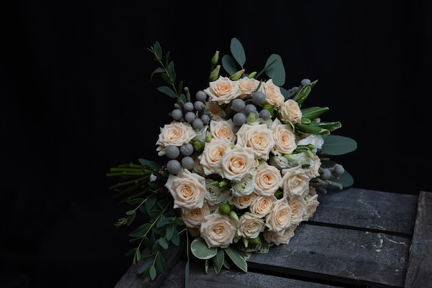 Schöner Hochzeitsblumenstrauß der buschigen Sahnerose, des Eukalyptus, des Brunei, des Pittosporum und des Lisianthus auf einer schwarzen Wand.