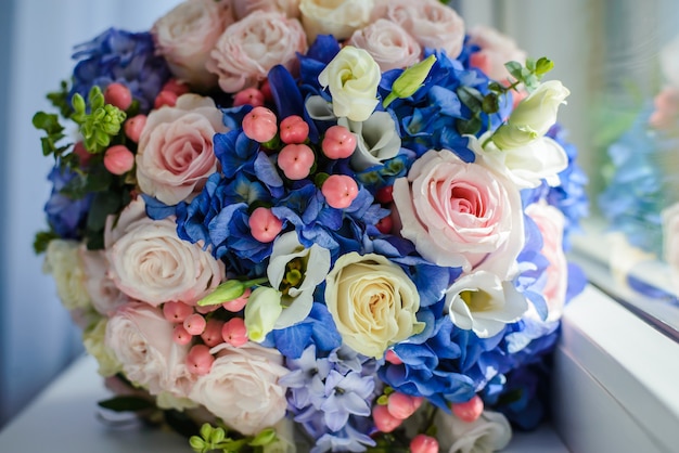 Schöner Hochzeitsstrauß aus blauen und rosa Blumen, Rosen am Fenster liegen