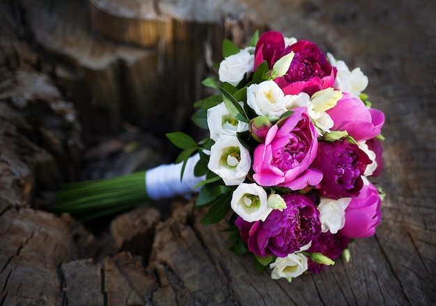 Schöner Hochzeitsstrauß mit bunten Blumen, die auf einem Baumstumpf liegen.