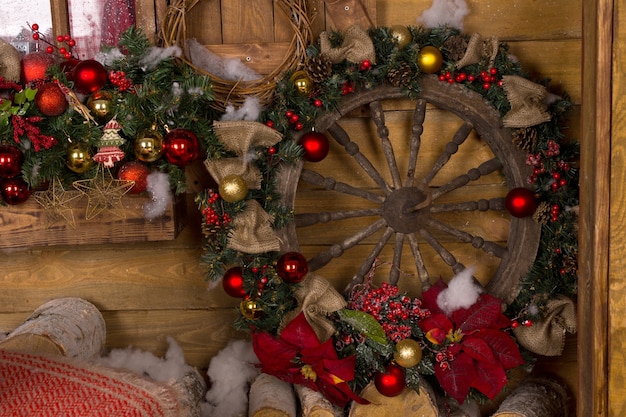 Schöner hölzerner nautischer Schiffsrad-Weihnachtskranz, mit roten Blumen, braunen Bändern und roten und goldenen Kugeln, gelehnt an hölzerner Wand.