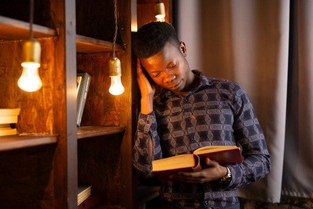 schöner junger afrikanischer Mann, der Buch in der Bibliothek liest