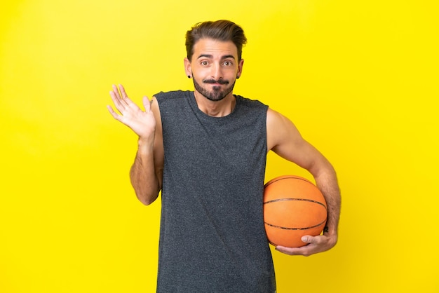 Schöner junger Basketballspieler, isoliert auf gelbem Hintergrund, der Zweifel hat, während er die Hände hebt