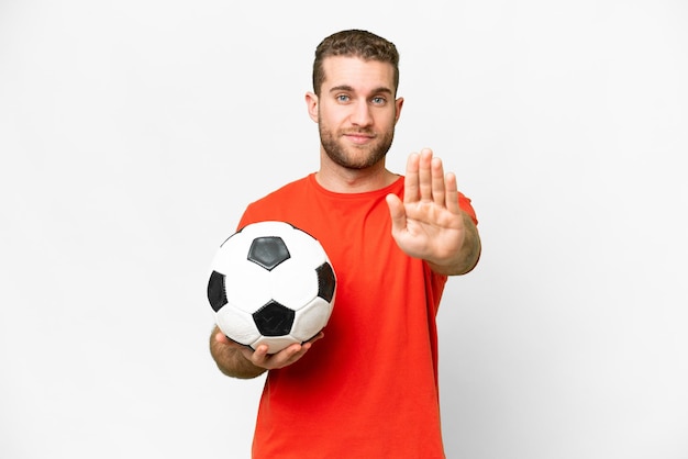 Schöner junger Fußballspieler mit isoliertem weißem Hintergrund, der eine Stopp-Geste macht
