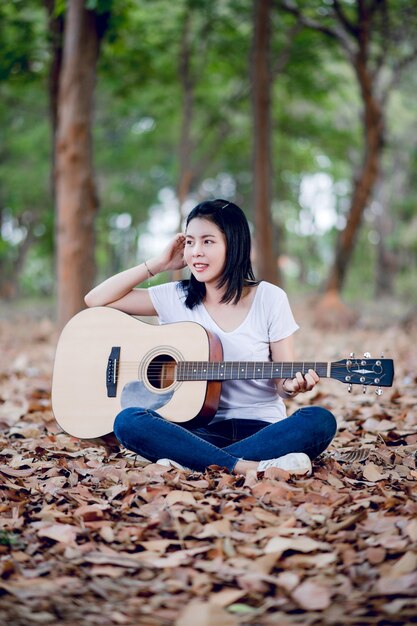 Schöner junger Gitarrist, der glücklich Gitarre im Garten, im Naturwald, im Musikkonzept spielt