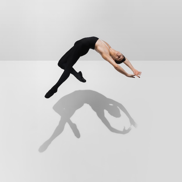 Schöner junger männlicher Athlet, der auf weißem Studiohintergrund mit Schatten im Sprung, Luftfliegen übt