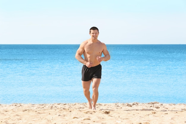 Schöner junger Mann, der am Meeresstrand läuft