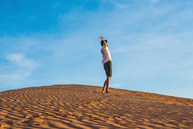 Schöner junger Mann, der barfuß auf Sand in der Wüste springt und die Natur und die Sonne genießt. Spaß, Freude und Freiheit.