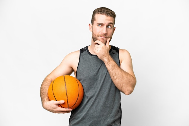 Schöner junger Mann, der Basketball vor isoliertem weißem Hintergrund spielt und Zweifel hat und nachdenkt