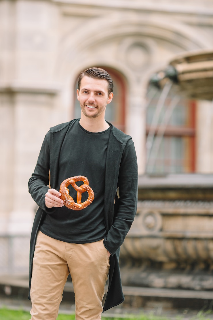 Foto schöner junger mann, der brezel hält und im park sich entspannt