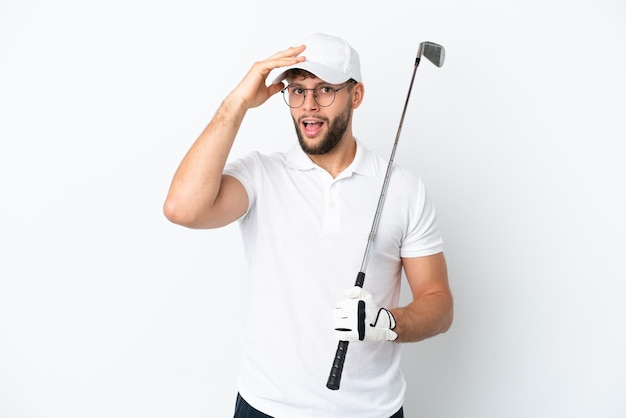 Schöner junger Mann, der isoliert auf weißem Hintergrund Golf spielt und dabei eine Überraschungsgeste macht, während er zur Seite schaut