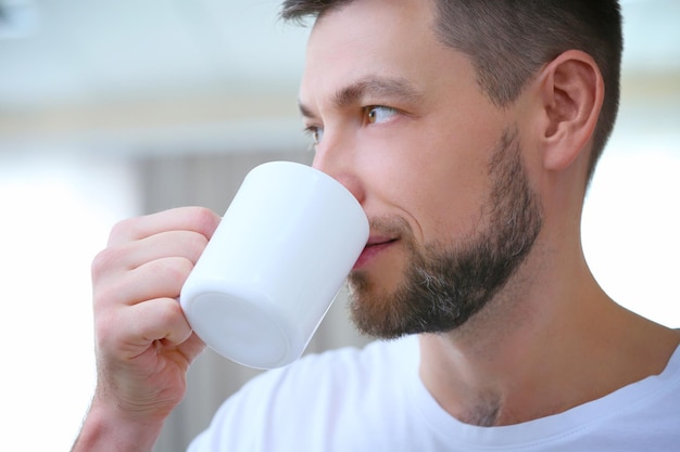 Schöner junger Mann, der zu Hause Kaffee trinkt, Nahaufnahme