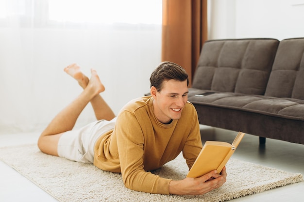 Schöner junger Mann in gelber Freizeitkleidung, der zu Hause sitzt und ein Buch liest