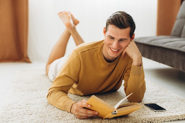 Schöner junger Mann in gelber Freizeitkleidung, der zu Hause sitzt und ein Buch liest