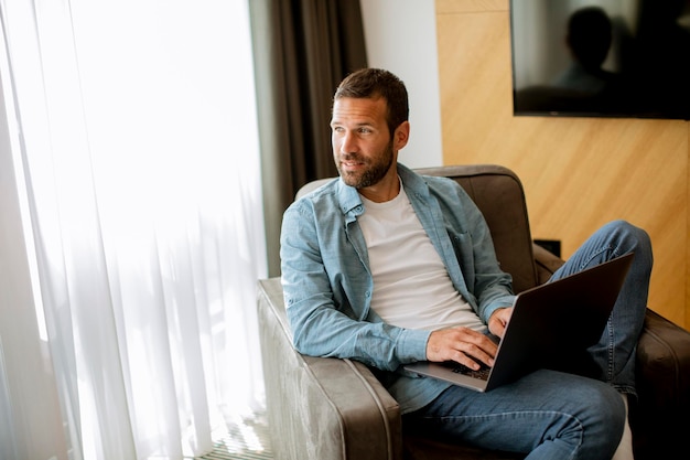 Schöner junger Mann mit Laptop-Computer im Wohnzimmer