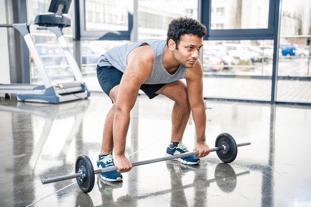 Schöner junger Mann trainiert mit Langhantel im Fitnessstudio