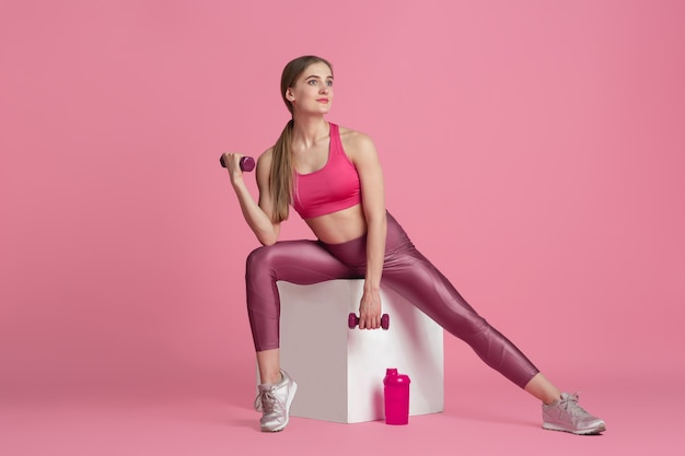 Schöner junger weiblicher Athlet, der auf monochromem Porträt der rosa Studiowand übt
