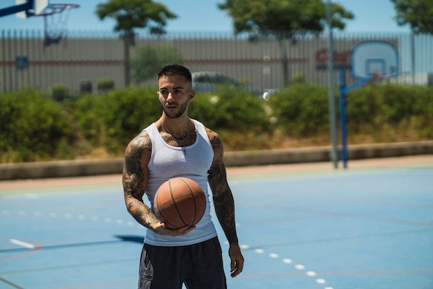 Schöner kaukasischer Basketballspieler mit coolen Tattoos, der auf dem Platz steht und den Ball hält