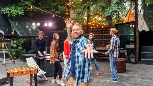 Foto schöner kaukasischer junger mann tanzt in der nähe der kamera auf dem hintergrund seiner freunde an der