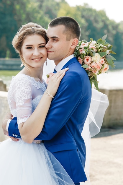 Schöner Kerl und Mädchen, Braut in einem weißen Hochzeitskleid, Bräutigam in einer klassischen blauen Klage gegen einen Naturhintergrund. Hochzeit, Familiengründung.