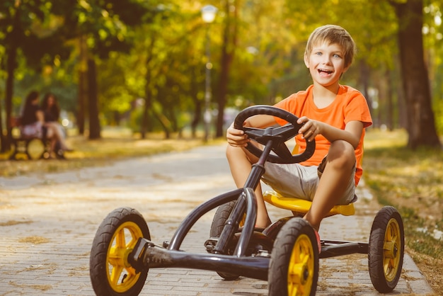 Schöner kleiner Junge, der Spielzeugauto im Sommerstadtpark reitet