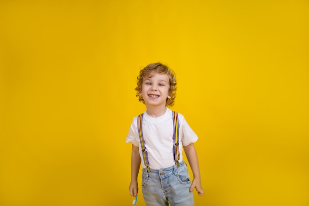 schöner kleiner lockiger Junge auf gelbem Hintergrund steht mit einer Zahnbürste lächelnd