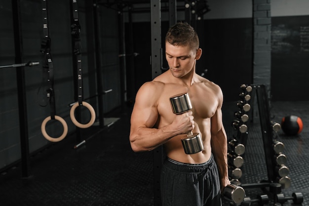 Schöner, kraftvoller Bodybuilder, der Übungen mit Hanteln in einem Fitnessstudio macht. Muskulöser Körper der Eignung auf dunklem Hintergrund.